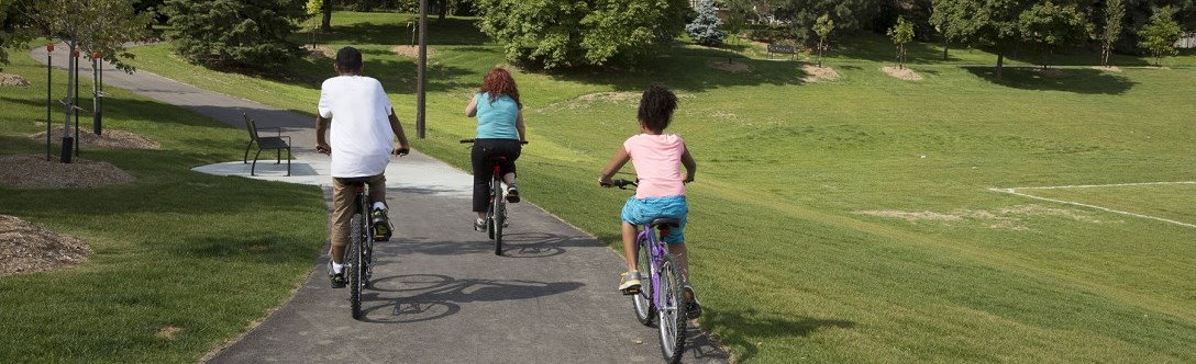 Three people riding a bike on a paved pathway